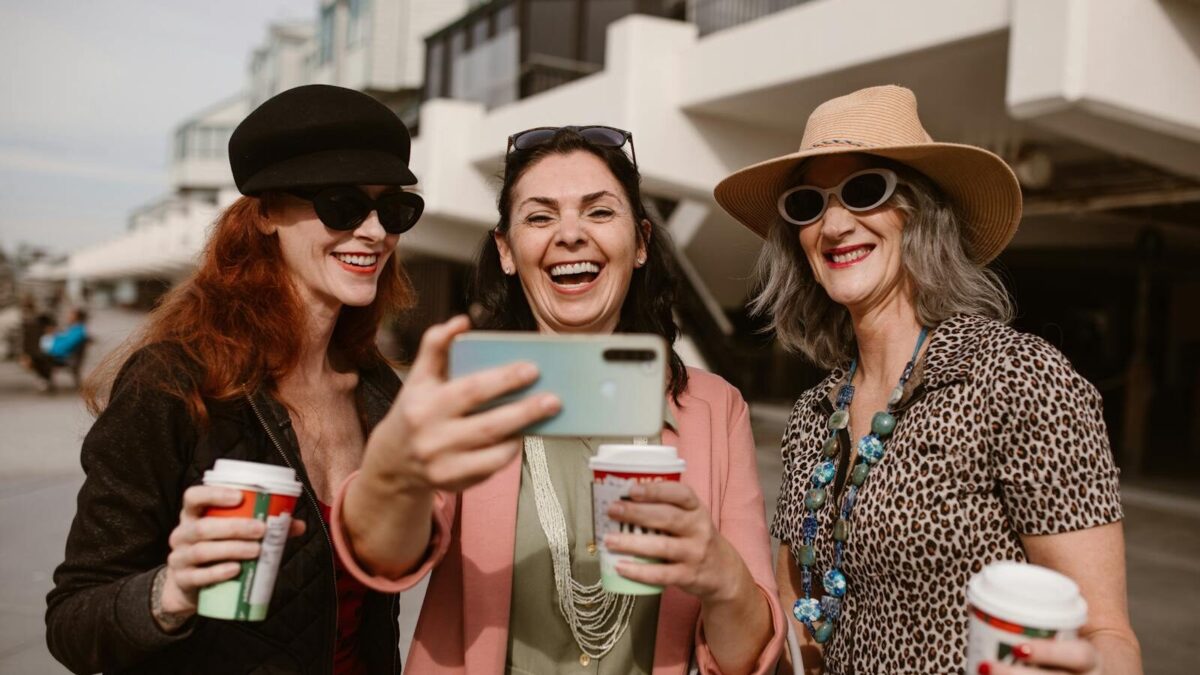 Three happy women taking a selfie outdoors while enjoying coffee together.