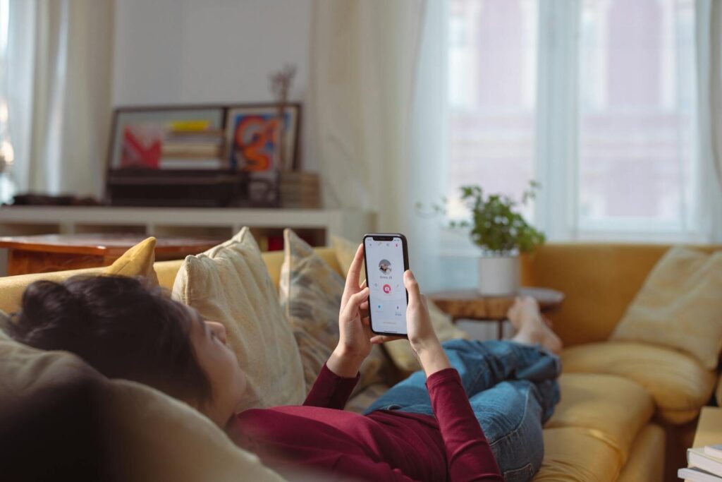 Woman relaxing and using a dating app on her smartphone while lying on a sofa indoors.