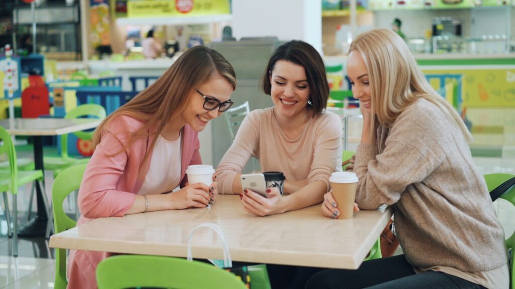 Three women looking at a smartphone at a cafe.