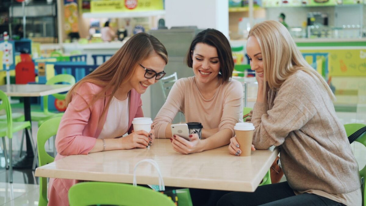 Three women looking at a smartphone at a cafe.
