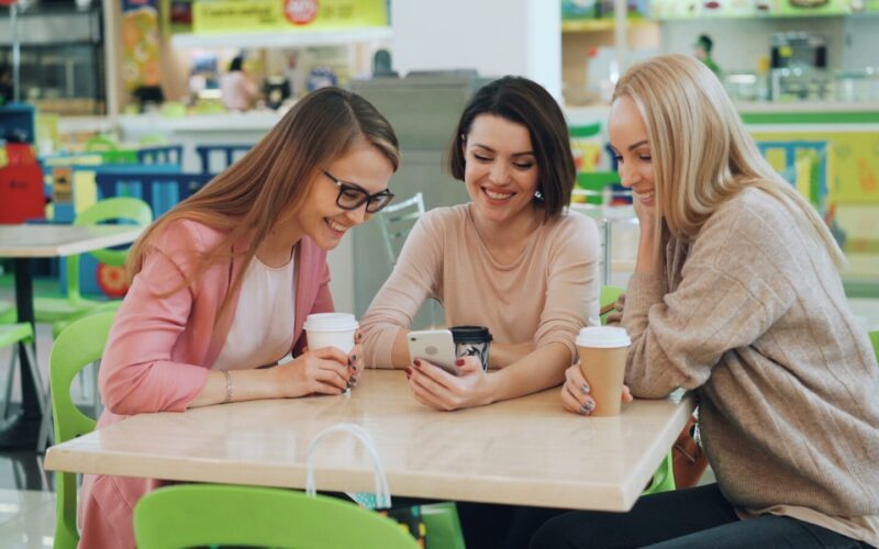 Three women looking at a smartphone at a cafe.