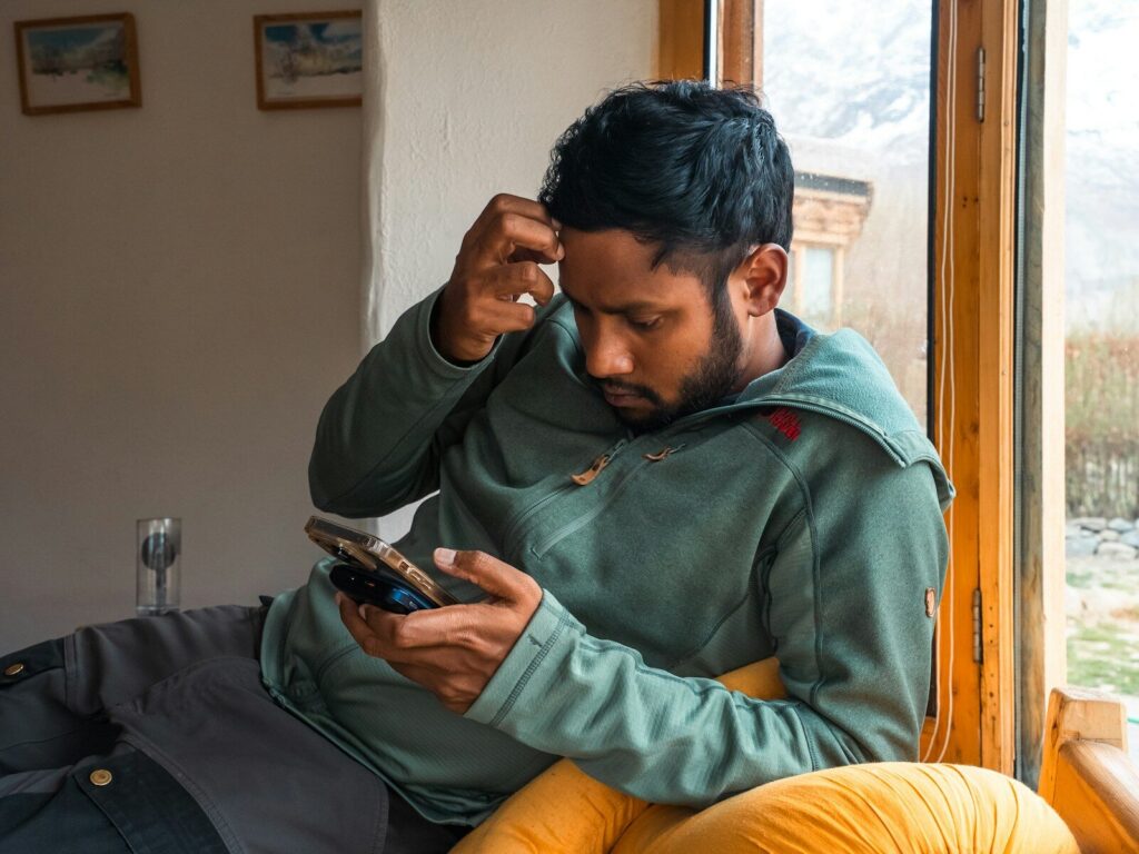 Man is looking at his phone, seemingly puzzled.