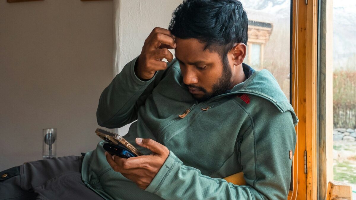 Man is looking at his phone, seemingly puzzled.