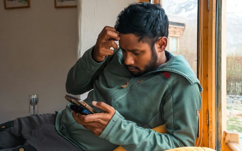 Man is looking at his phone, seemingly puzzled.