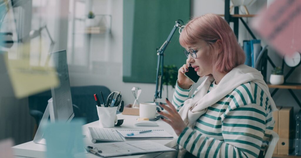 A woman sitting at a desk talking on a cell phone