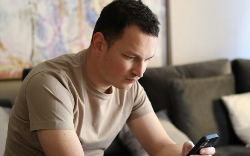a man sitting on a couch looking at his cell phone