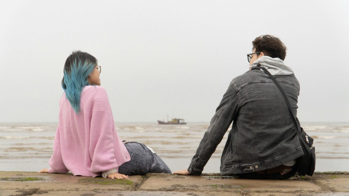 a man and a woman sitting on the edge of a pier