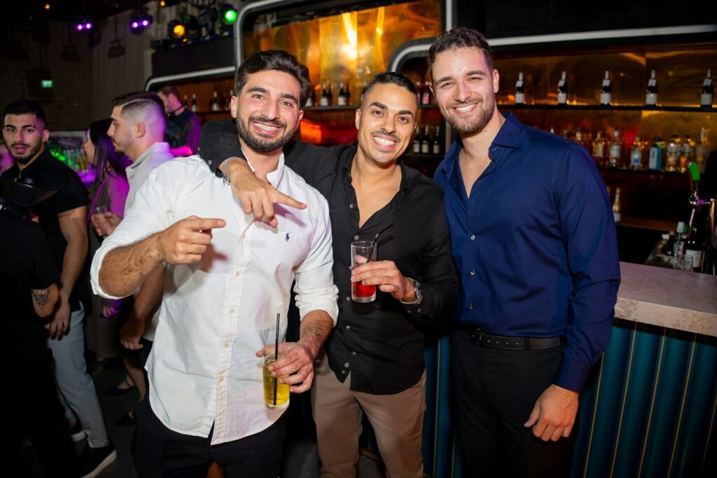 Three smiling men holding drinks in a nightclub.