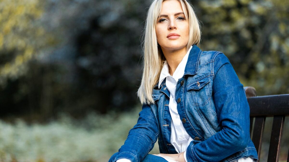 woman in blue denim jacket sitting on brown wooden bench during daytime