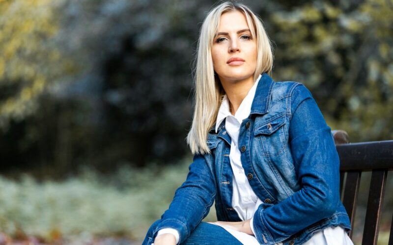 woman in blue denim jacket sitting on brown wooden bench during daytime