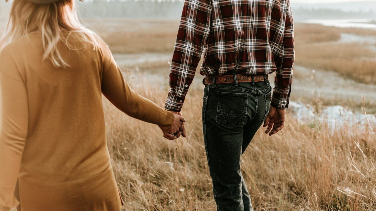 man and woman walking along grass field while holding hands