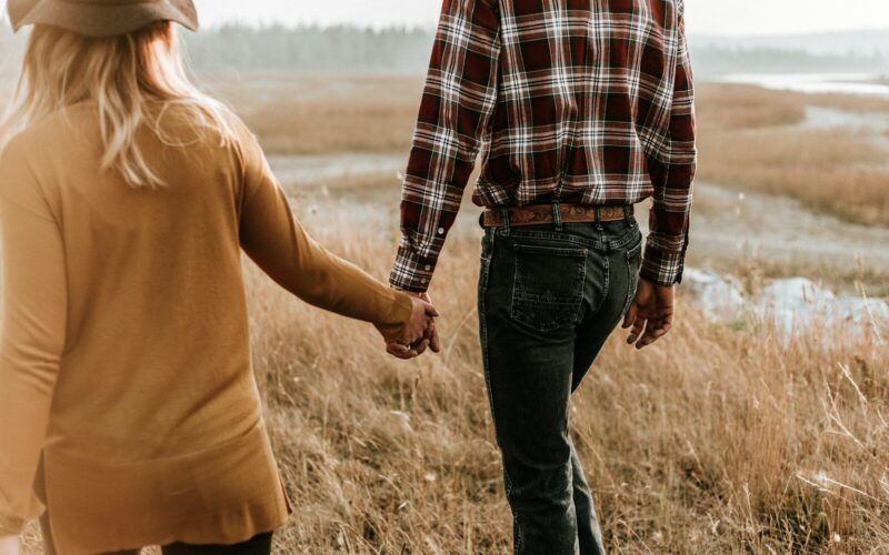 man and woman walking along grass field while holding hands