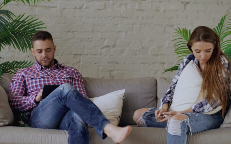 Couple sitting on sofa looking at phones