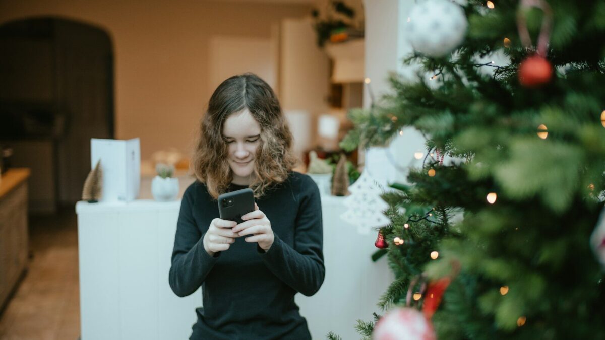 a woman standing in front of a christmas tree looking at her cell phone