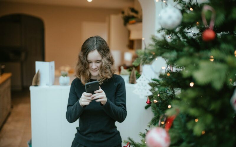 a woman standing in front of a christmas tree looking at her cell phone