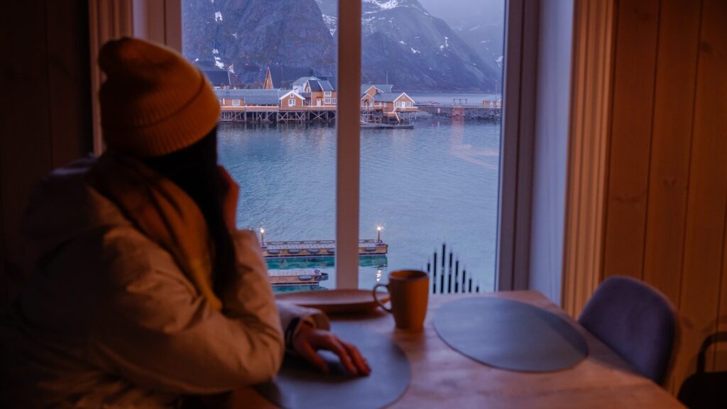 Woman looking out window at harbor and mountains.