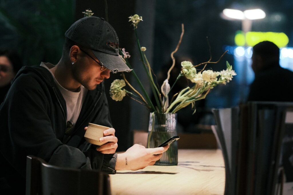 Man in hat looking at phone at cafe table.