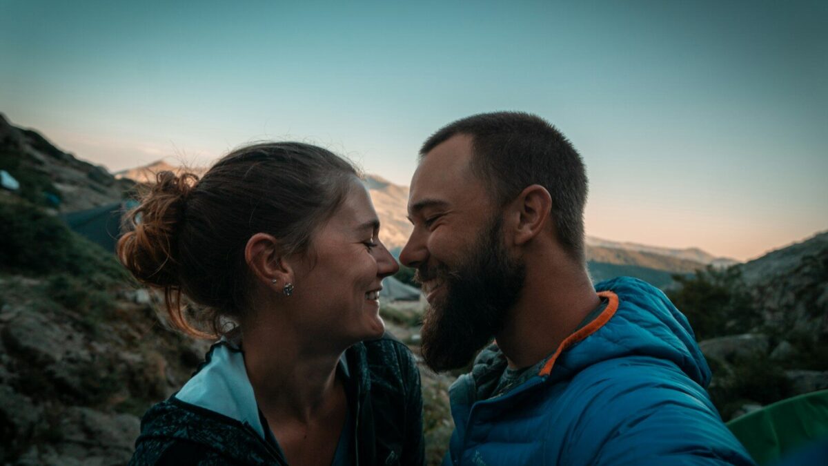 man in blue hoodie kissing woman in black and gray shirt during daytime