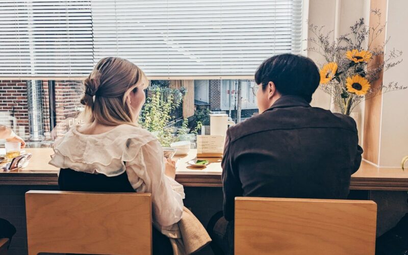 a man and a woman sitting at a table in front of a window