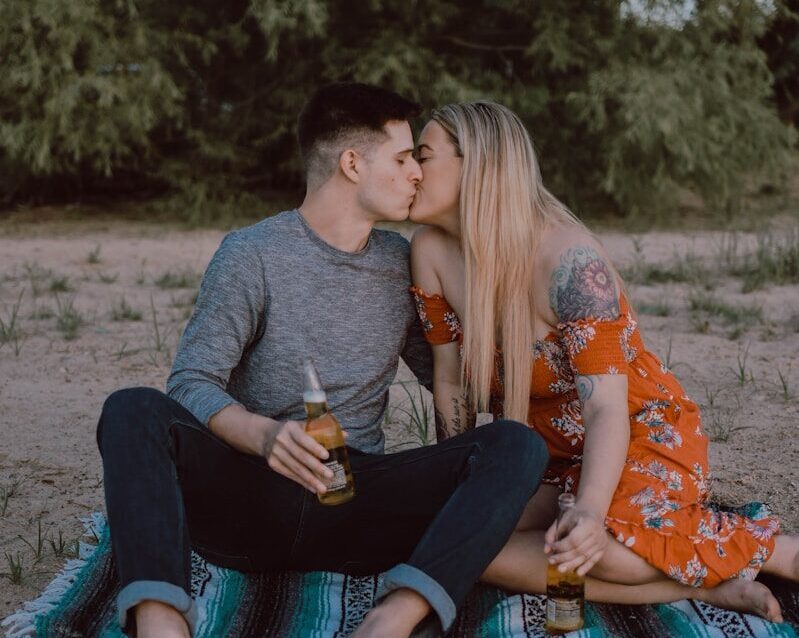 man and woman sitting while kissing on ground